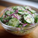 Close-up van een kom van romige komkommersalade met dille en rode ui.