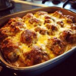 Gegrilde gehaktballen bedekt met gesmolten kaas in een ovenschotel, onderdeel van een Sausage Gravy Biscuit Pie.