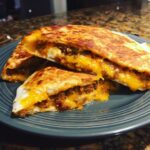 Twee helften van Sheet Pan Quesadillas met overvloedig gesmolten kaas en gekruid gehakt.