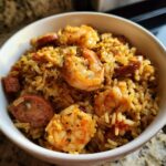 Close-up van een kom met Shrimp and Sausage Dirty Rice, vol met garnalen, worst en rijst.