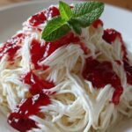Close-up van Spaghetti Ice Cream Delight, versierd met rode aardbeiensaus en een muntblaadje.