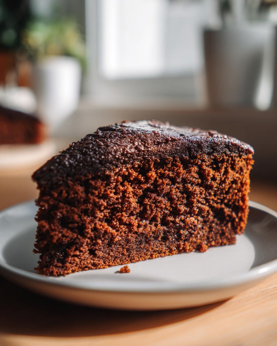 Een dikke, sappige plak Super Vochtige Peperkoek Cake op een grijs bord, met een zachte textuur.