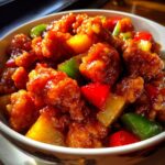 Close-up of a bowl filled with glistening Sweet and Sour Chicken, pineapple chunks, and bell peppers.