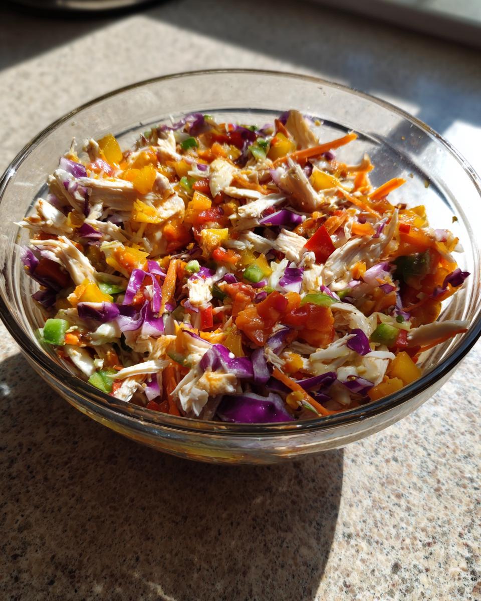 A close-up of the Ultimate BBQ Chicken Salad in a glass bowl, featuring shredded chicken, colorful bell peppers, red cabbage, and carrots.