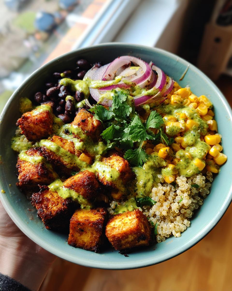 A close-up of a Zesty Cilantro Lime Tofu Bowl, featuring golden-brown tofu cubes, black beans, corn, quinoa, red onion, and a vibrant cilantro-lime dressing.