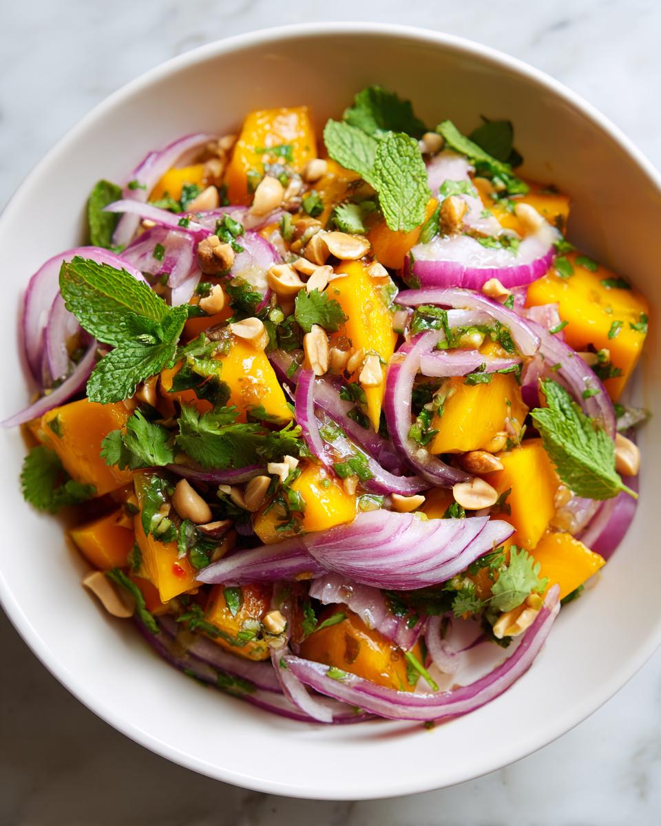 A vibrant bowl of Zesty Mango Salad With A Thai Twist, featuring diced mango, red onion, mint, cilantro, and peanuts.
