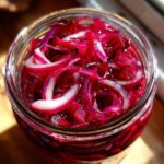 Close-up of Zesty Pickled Red Onions in a glass jar, showcasing vibrant pink and white slices.