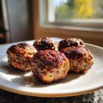 Five golden-brown, slightly caramelized Air Fryer Meatballs resting on a white plate, lit by natural sunlight.