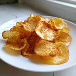 A close-up of a pile of golden, crispy Air Fryer Potato Chips seasoned with paprika on a white plate.