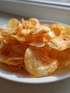 A white plate piled high with golden, crispy Air Fryer Potato Chips dusted with red seasoning.