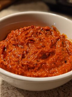 A close-up of vibrant, thick Ajvar Roasted Red Pepper Spread filling a small white bowl.
