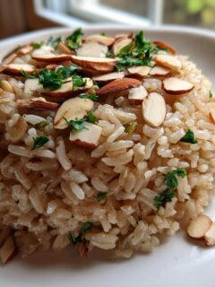 A molded serving of Almond Brown Rice Pilaf topped with sliced almonds and fresh parsley on a white plate.