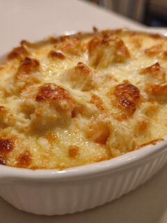 Close-up of a bubbly, golden-brown Baked Shrimp Dip served hot in a white ceramic dish.