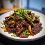 A close-up shot of perfectly caramelized Beef Bulgogi slices garnished with sesame seeds and fresh green onions.