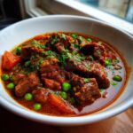 A close-up of hearty Beef Stew With Sweet Peas And Tomatoes in a white bowl, garnished with fresh parsley.