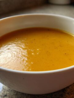 Close-up of a creamy, orange-yellow bowl of Beer Cheddar Cheese Soup resting on a granite countertop.