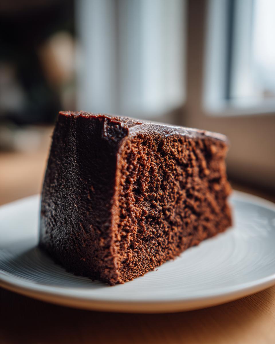 Close-up of a thick, moist slice of Black Magic Chocolate Cake on a white plate.