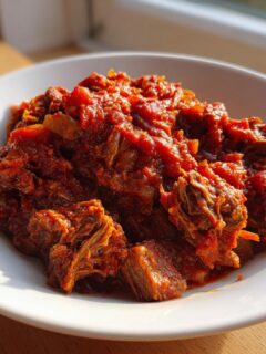 A close-up of rich, slow-cooked Braised Steak Ragu served in a white bowl, glistening in sunlight.