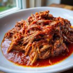 Close-up of tender, shredded beef coated in a thick, vibrant red tomato sauce, representing the Braised Steak Ragu.