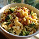 A close-up of creamy Broccoli Bacon Macaroni And Cheese served in a white bowl, topped with crispy bacon bits.