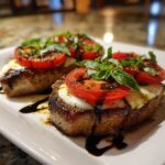 Two perfectly cooked Caprese Pork Chops topped with melted mozzarella, sliced tomatoes, and fresh basil.