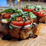 Two thick Caprese Pork Chops topped with melted mozzarella, roasted tomatoes, fresh basil, and balsamic glaze.