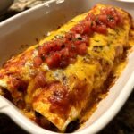 Close-up of baked Breakfast Enchiladas covered in melted cheddar cheese and topped with fresh pico de gallo.