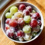 A close-up of a bowl filled with red and green grapes coated in a creamy dressing, part of an Irresistible Chicken Salad Chick Grape Salad recipe.