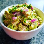 Close-up of a white bowl filled with Creamy Avocado Tuna Salad, topped with red onion and cilantro.