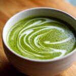 Close-up of vibrant green Broccoli Potato Soup topped with a white cream swirl garnish.
