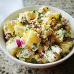 A close-up of creamy potato salad with egg, red onion, and fresh dill, sprinkled with red pepper flakes.