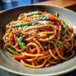 A close-up of a delicious pasta dish with spaghetti, green beans, red peppers, and grated cheese.