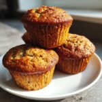 A stack of three freshly baked Delightful Fathers Day Banana Muffins on a white plate, golden brown and inviting.