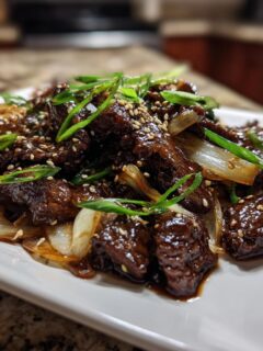 Close-up of savory Beef Bulgogi pieces glazed in sauce, served with caramelized onions and topped with sesame seeds and green onions.