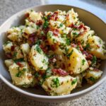 Close-up of a bowl of flavorful warm German potato salad topped with crispy bacon bits and fresh parsley.