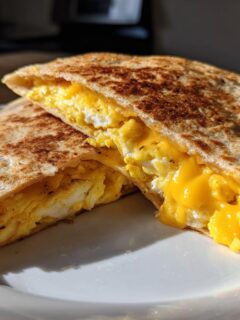 Close-up of a toasted Breakfast Quesadillas cut in half, revealing fluffy scrambled eggs and melted cheddar cheese inside.