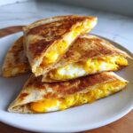Close-up of stacked, golden-brown Breakfast Quesadillas filled with fluffy scrambled eggs and melted cheddar cheese.