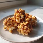 A pile of Irresistible Caramel Popcorn Balls glistening with caramel on a light pink plate.