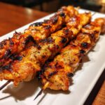 Close-up of perfectly grilled, juicy chicken skewers with char marks, seasoned with herbs, ready for a summer meal.