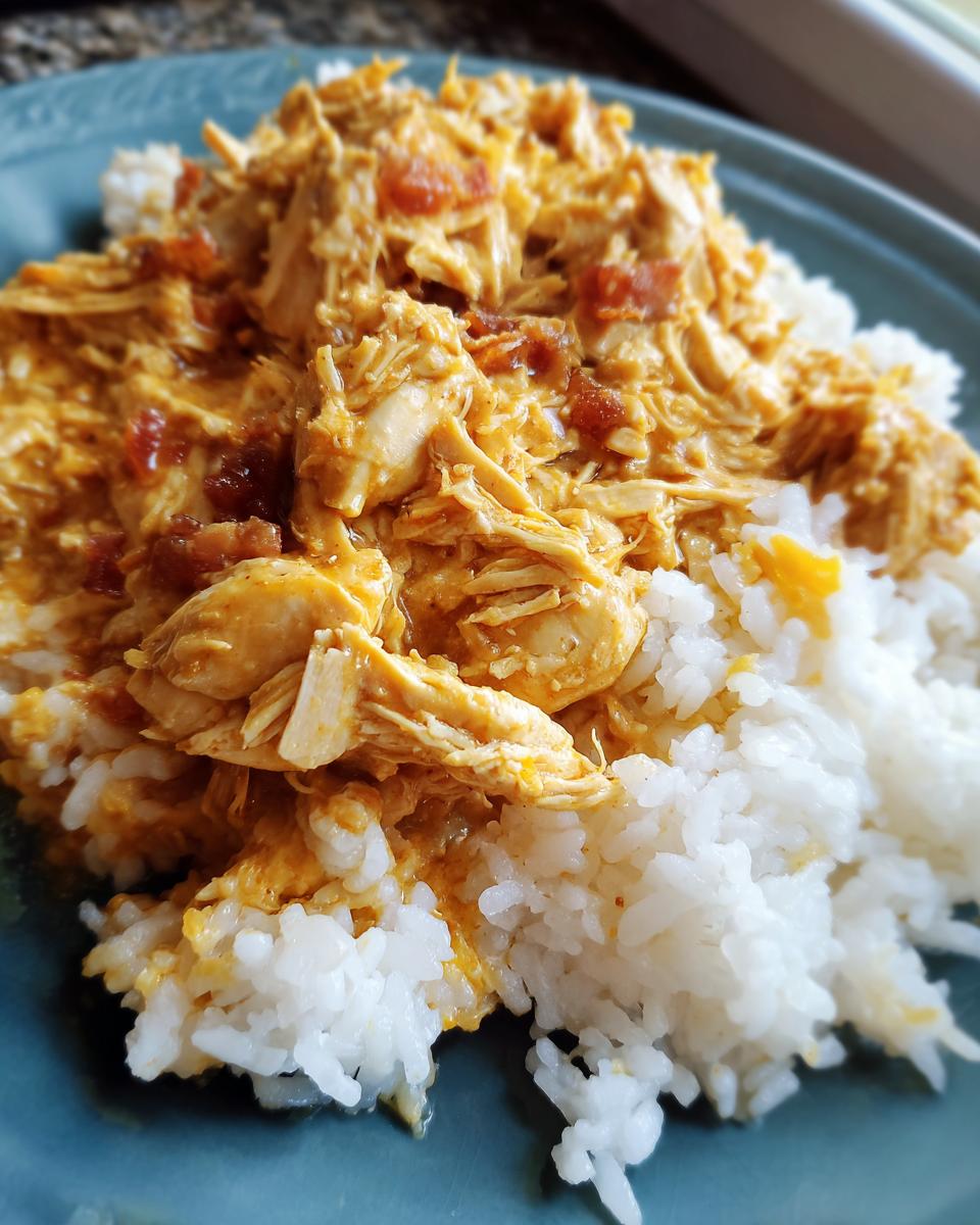 A close-up of Irresistible Crockpot Crack Chicken and Rice served on a blue plate, showing shredded chicken in a creamy sauce over white rice.