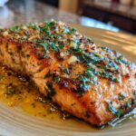 A close-up of an irresistible garlic butter salmon fillet, glistening with butter and topped with fresh parsley.