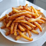 A close-up of a pile of Irresistible Homemade French Fries, lightly dusted with powdered sugar on a white plate.
