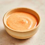 A small bowl filled with creamy, orange-pink Irresistible In And Out Sauce, speckled with spices.