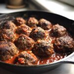 Close-up of Irresistible Smoked Italian Meatballs simmering in a rich tomato sauce in a cast-iron skillet.