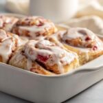 Close-up of irresistible strawberry cinnamon rolls baked in a white dish, generously drizzled with white icing.