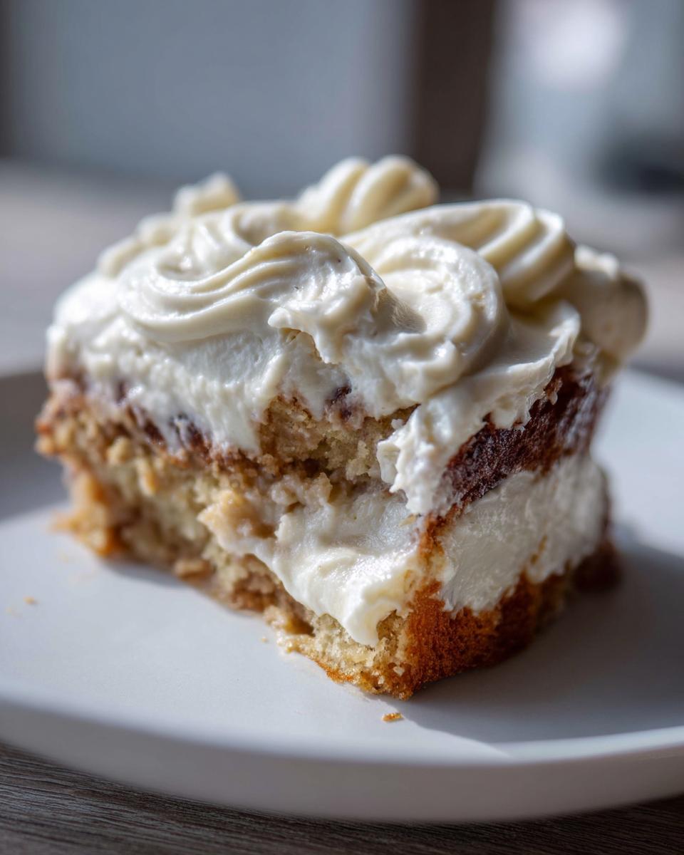A close-up of a moist slice of Banana Cake With Cream Cheese Frosting topped with piped swirls.