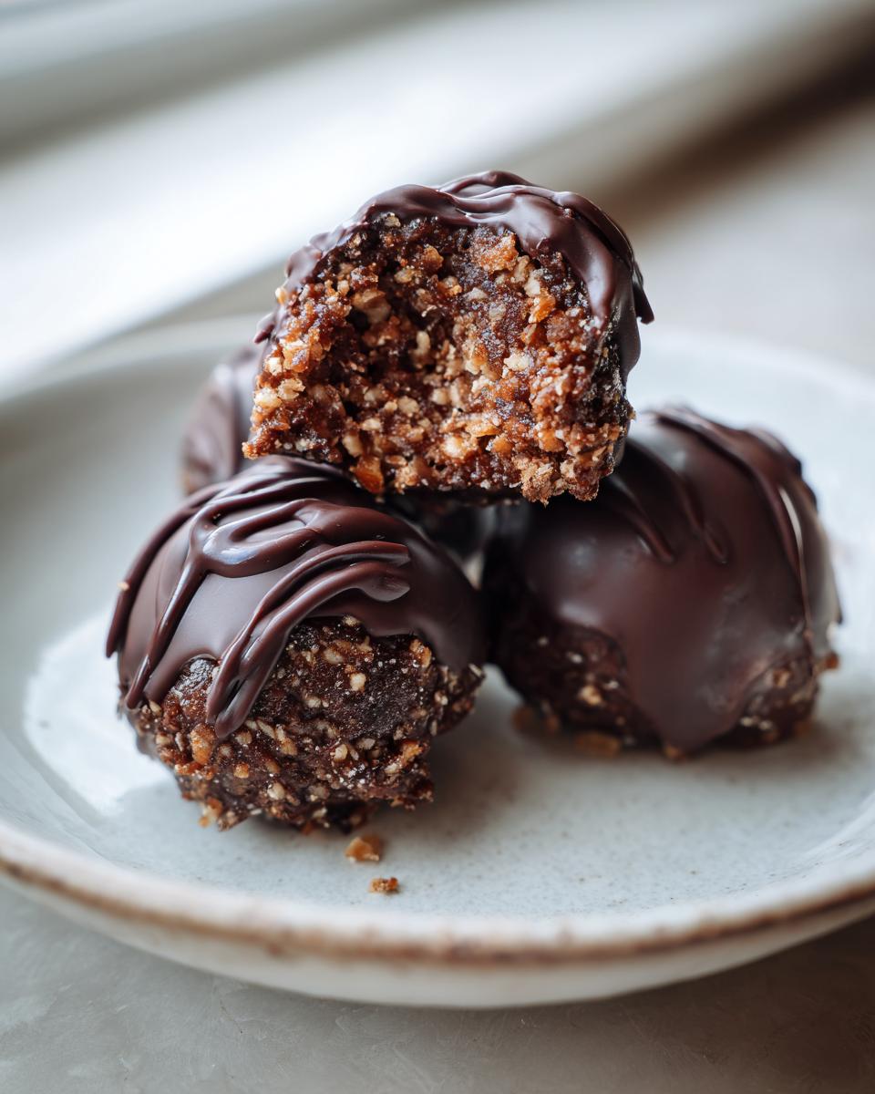 Three rich, chocolate-covered Bourbon Balls on a plate, one cut open showing the nutty interior.