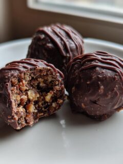 Three rich, chocolate-coated Bourbon Balls on a white plate, one cut open showing the nutty interior.