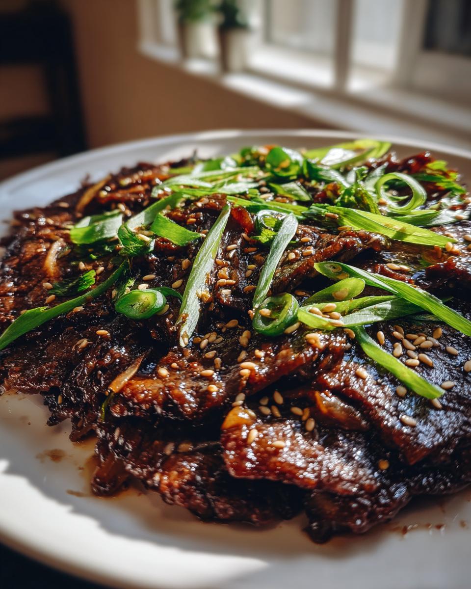 Close-up of glistening, dark marinated Beef Bulgogi served on a white plate and topped with fresh green onions and sesame seeds.
