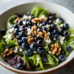 A close-up of a refreshing blueberry salad with walnuts and feta cheese on a bed of mixed greens.